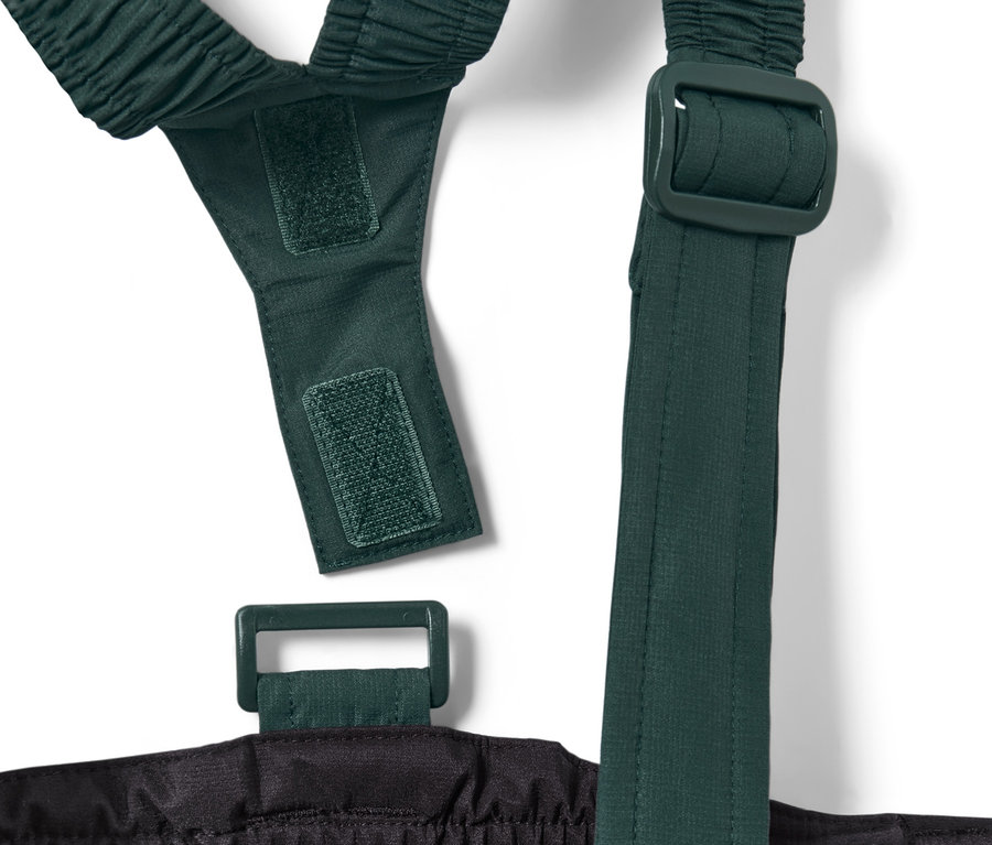 Detail dětských lyžařských kalhot, černé barvy, ukazující zelené nastavitelné popruhy a suchý zip.