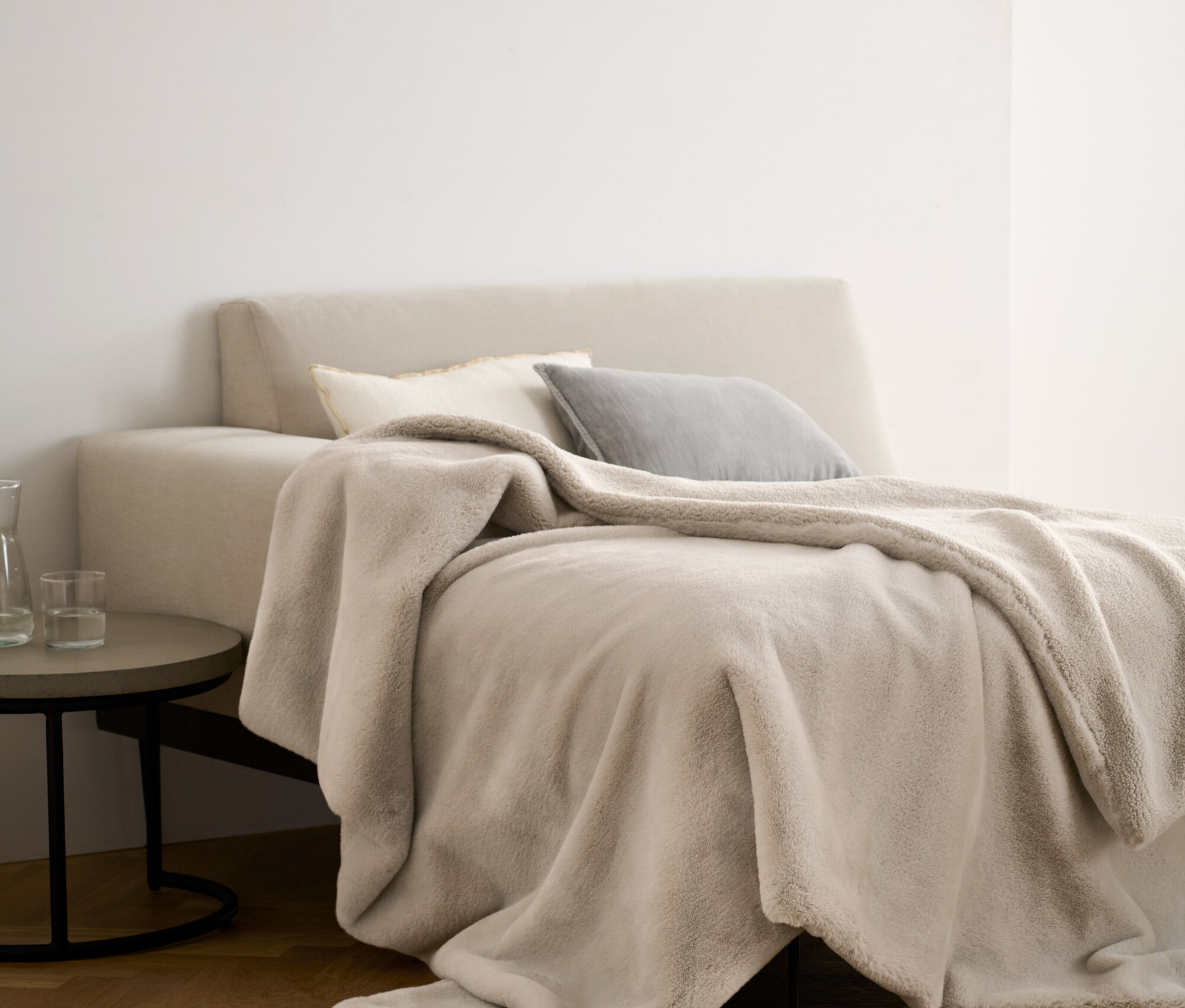 Béžová měkoučká deka z umělé kožešiny leží na posteli s polštáři.