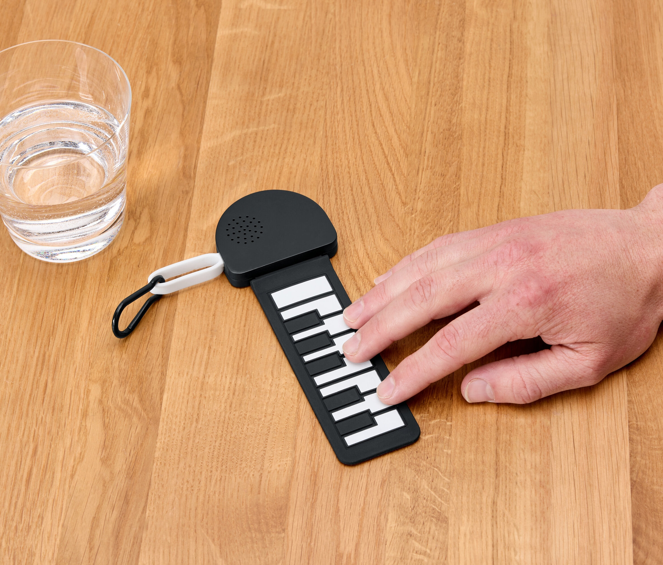 Ruka hraje na mini klavír vedle sklenice vody.