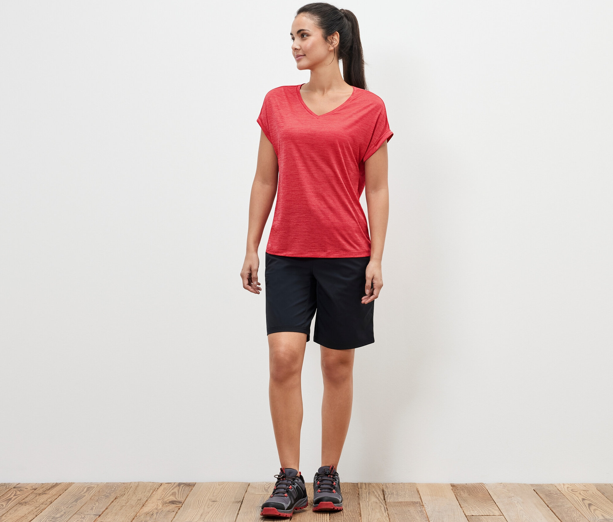 Žena stojí a má na sobě růžové funkční tričko a černé šortky.