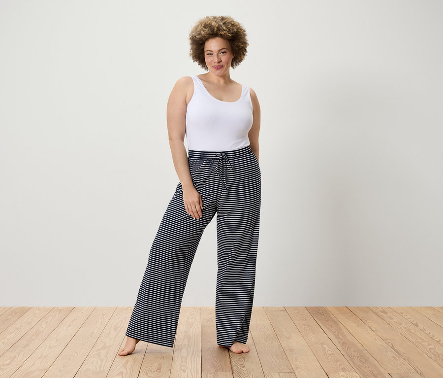 Žena pózuje v bílém tílku a pruhovaných kalhotech.