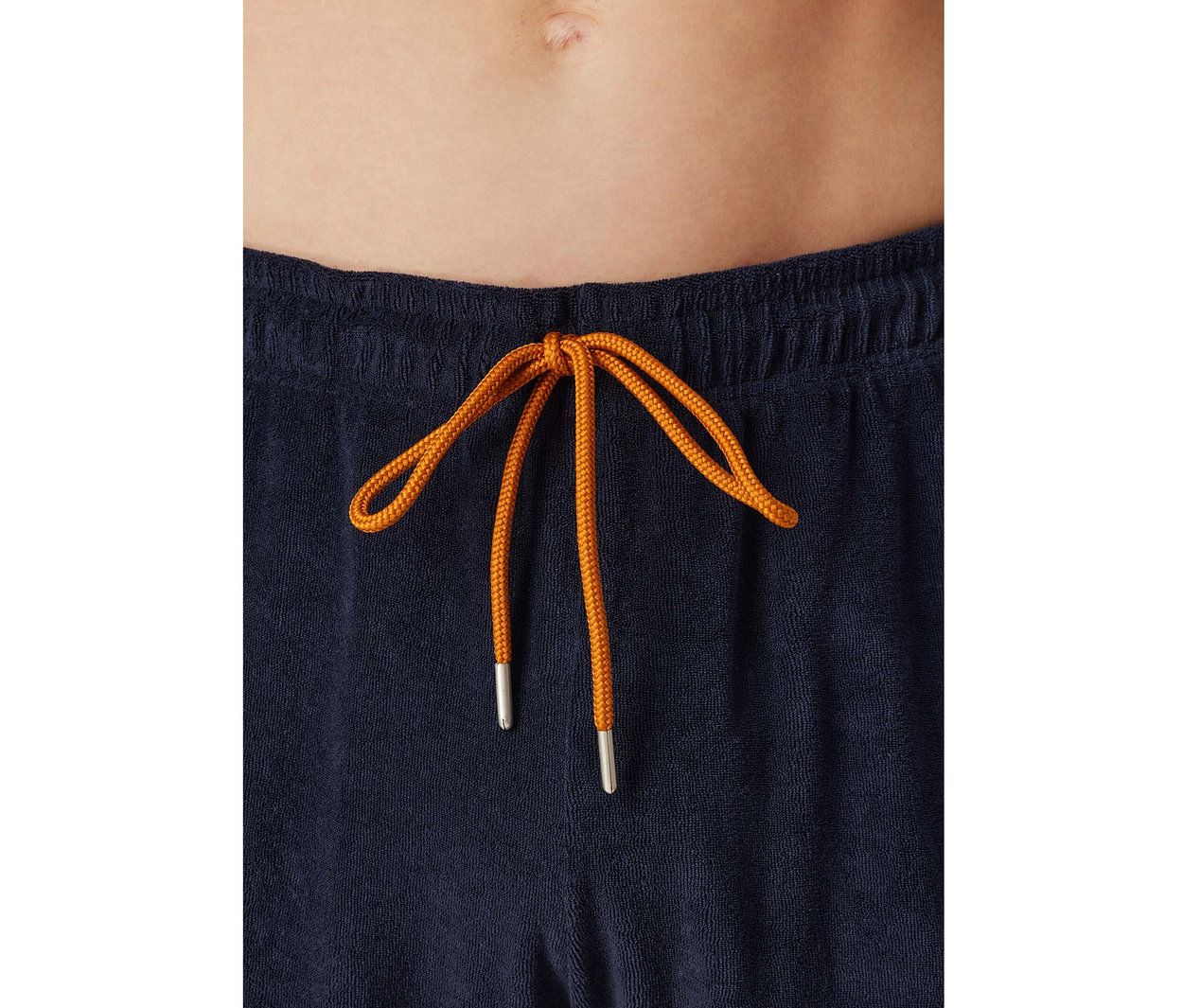 Detail břicha osoby v tmavě modrých froté pyžamových kalhotách SCHIESSER s oranžovou šňůrkou zavázanou na mašli.