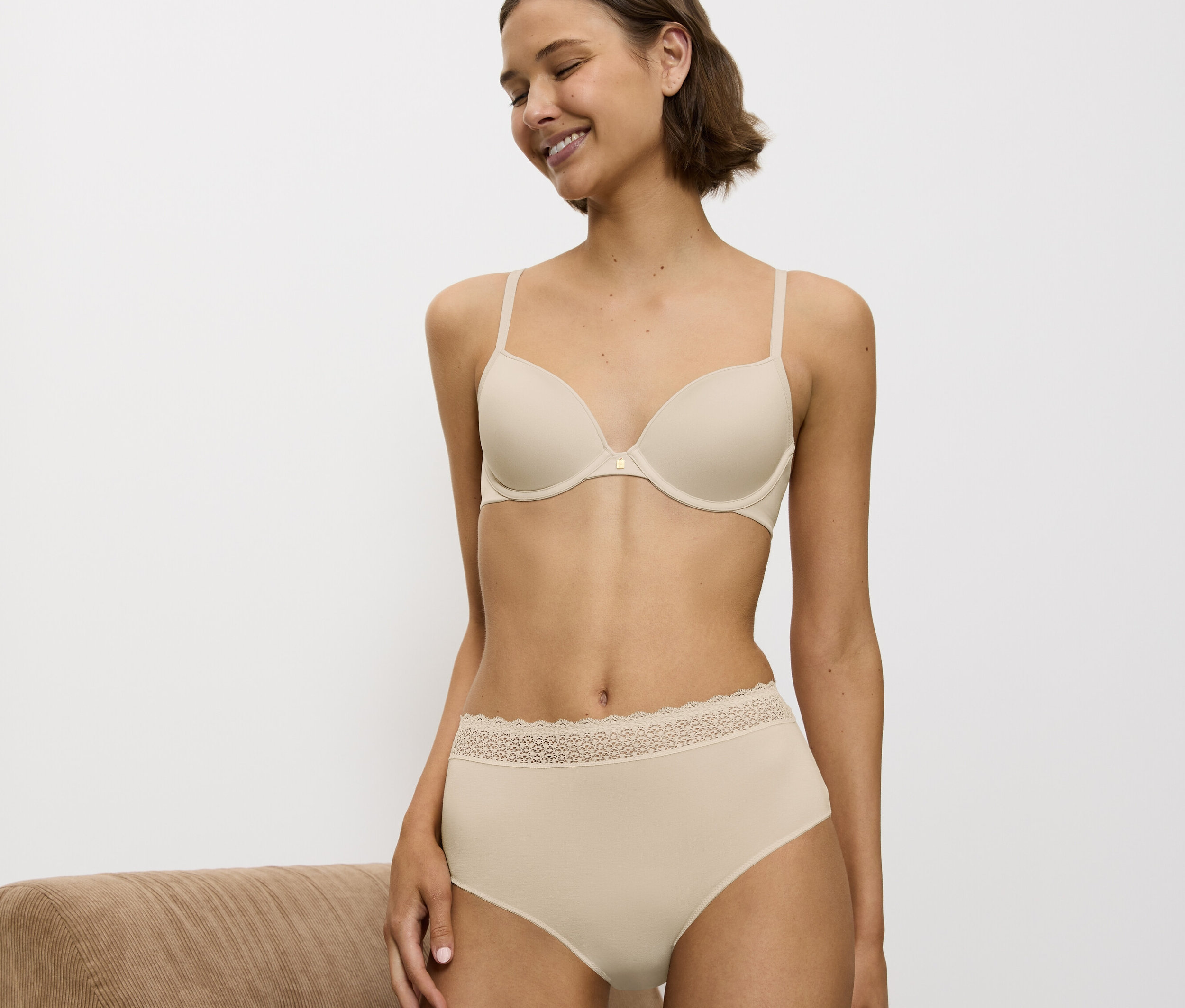 Žena usmívá se a nosí béžovou podprsenku a kalhotky s krajkou.