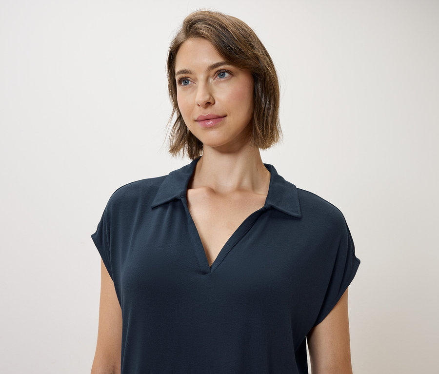 Žena s hnědými vlasy a modrýma očima má na sobě tmavě modré pološaty.