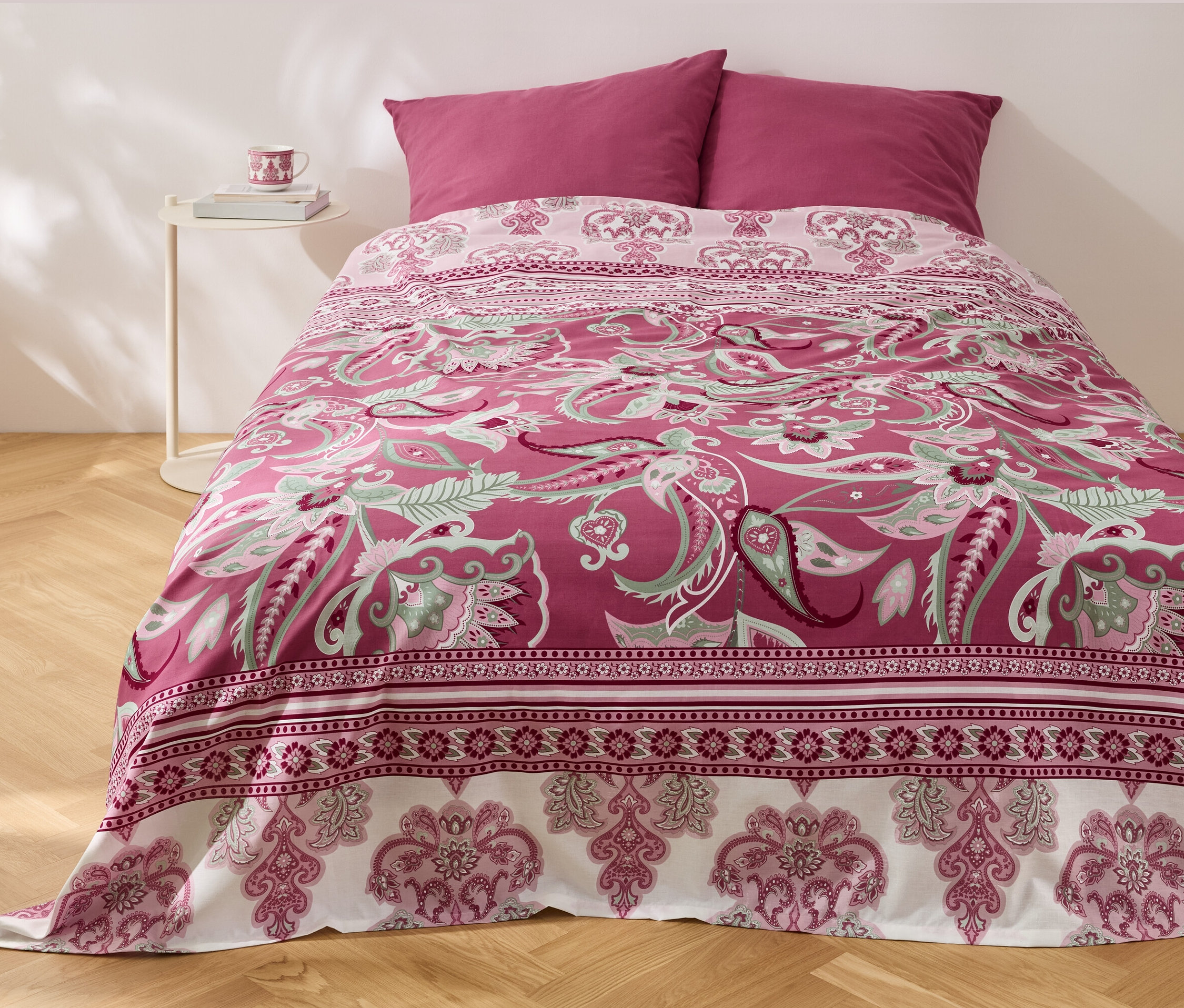 Na posteli leží multifunkční přehoz renforcé s květinovým vzorem a dva polštáře.