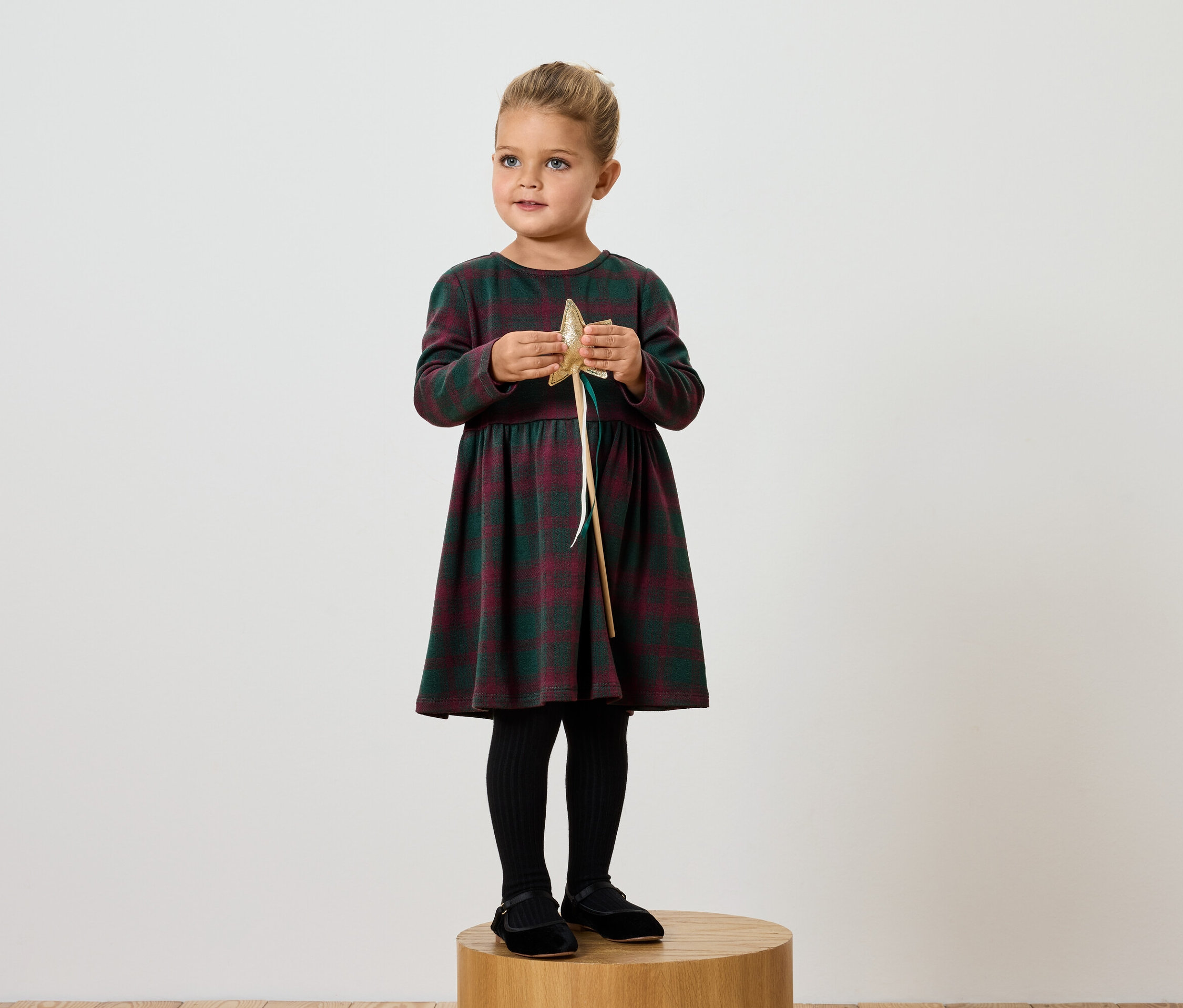 Dívka v kostkovaných šatech drží zlatou hvězdu.