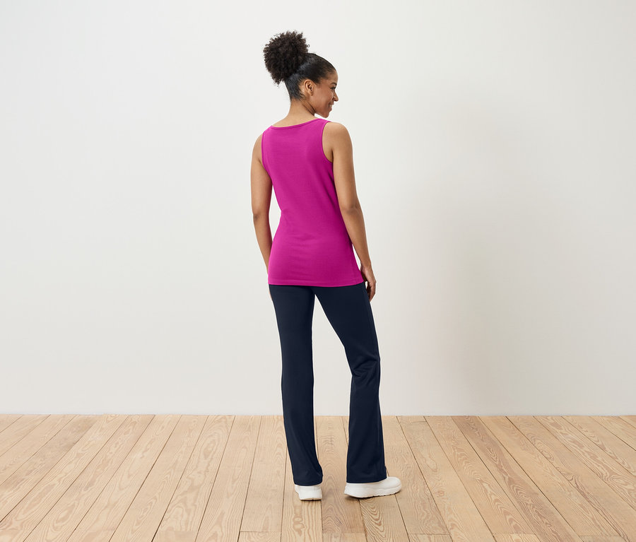 Žena stojí zády a má na sobě růžový top a tmavě modré kalhoty.