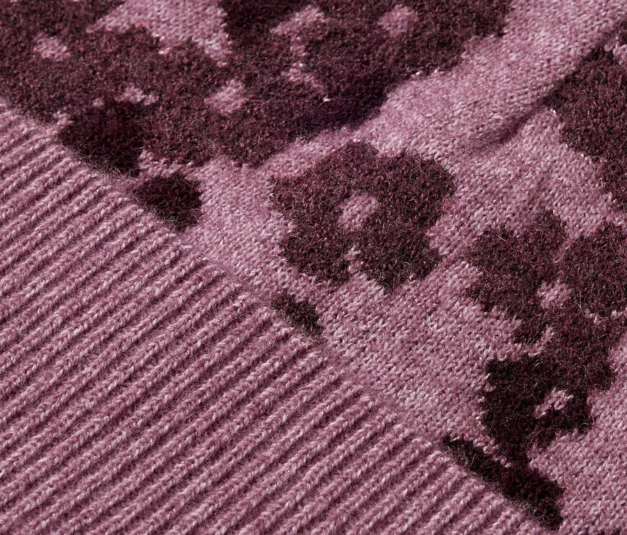 Detail fialového pleteného svetru s květinovým vzorem.
