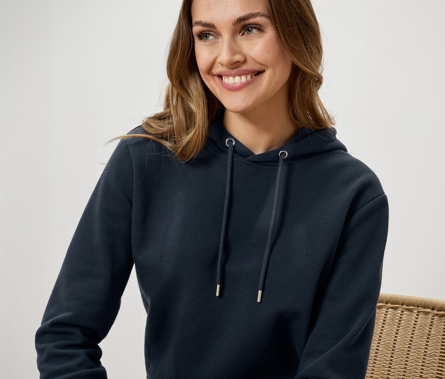 Usmívající se žena má na sobě tmavě modrou mikinu s kapucí.