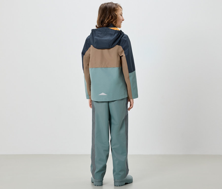 Dívka stojí zády a má na sobě barevnou bundu a dětské kalhoty do deště, šalvěj.