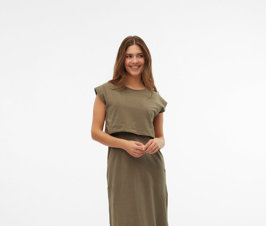 Žena má na sobě khaki šaty a krémové boty Mary Jane na bílém pozadí.