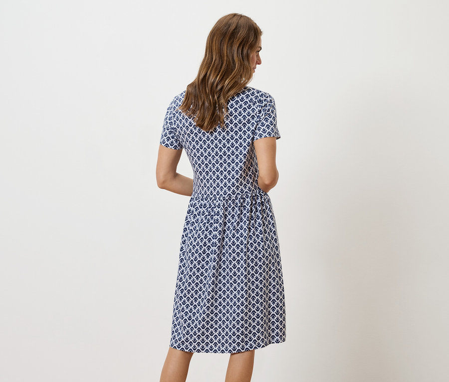 Žena stojí zády ke kameře a má na sobě modro-bílé vzorované šaty.