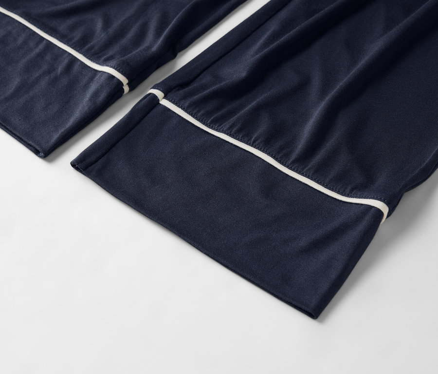 Detailní záběr na tmavě modré pyžamové kalhoty s bílým lemováním na bílém pozadí.