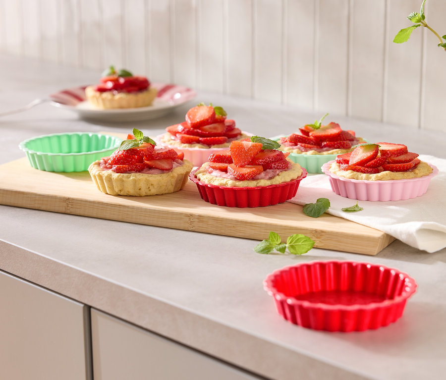 Několik jahodových košíčků v barevných formičkách na dřevěném prkénku, ozdobených mátou.