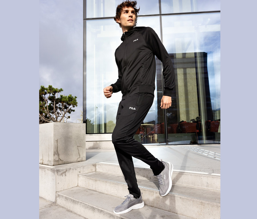 Muž v černé teplákové soupravě Fila sestupuje po betonových schodech, šedé boty Fila.