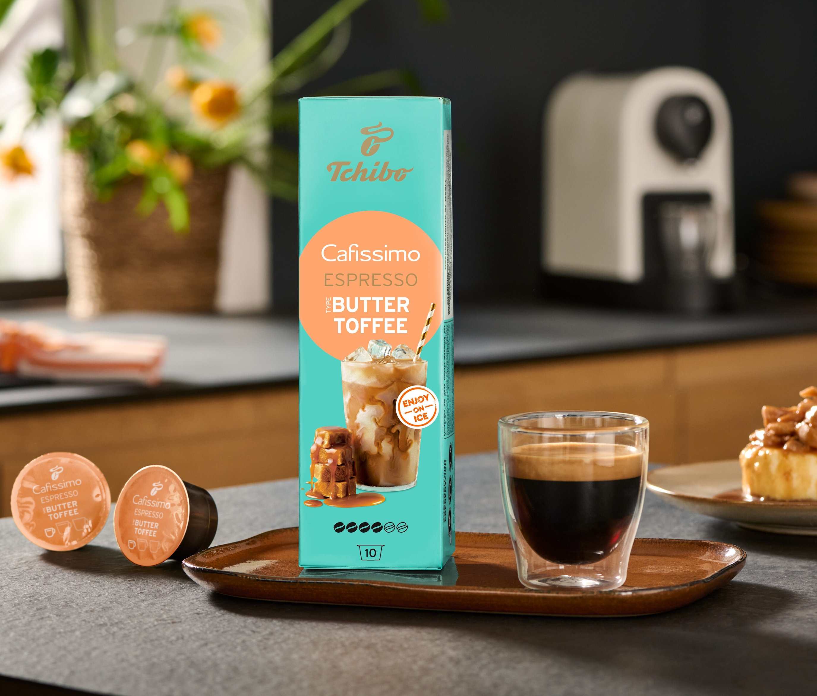 Balení Cafissimo Flavoured Espresso – Buttertoffee a kávovar Cafissimo pure+, white stojí na stole vedle šálku kávy.