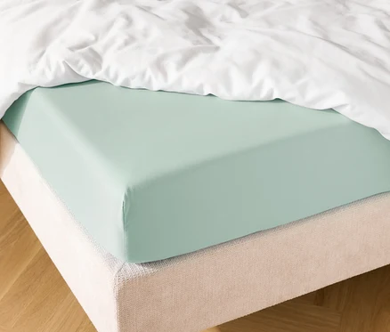 Detailní záběr postele se světle modrým prostěradlem a bílou přikrývkou.