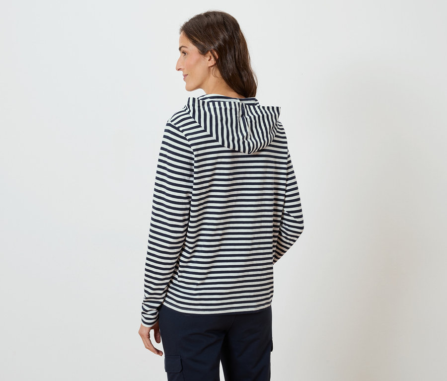 Žena zezadu, má na sobě pruhovanou mikinu s kapucí a tmavě modré kalhoty.