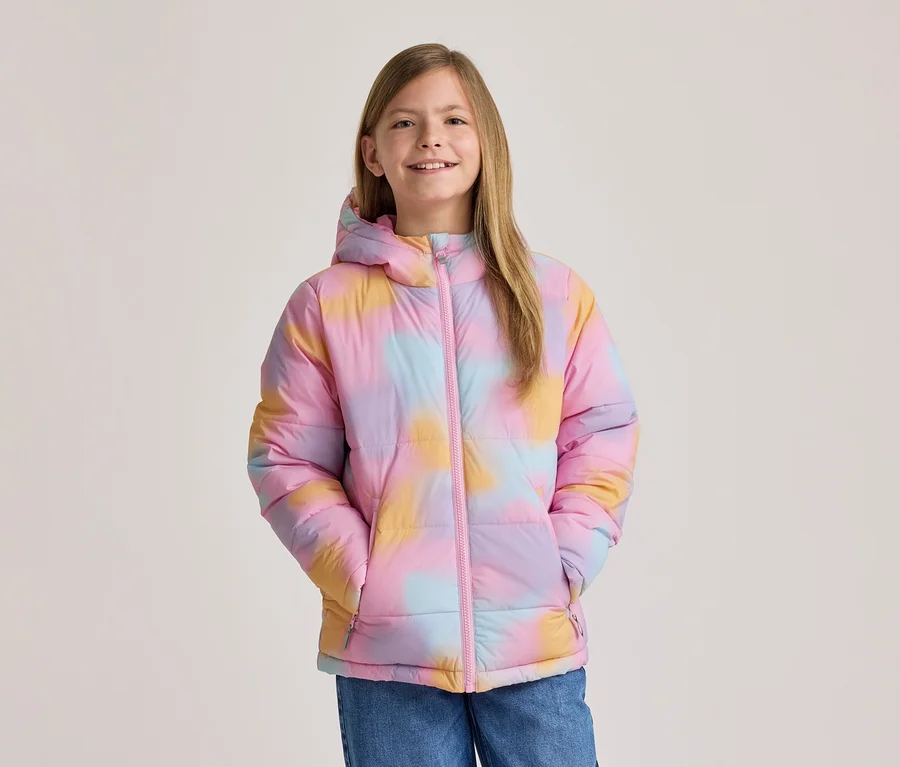 Usmívající se dívka v barevné tie-dye bundě v růžové, žluté a modré barvě s kapucí a růžovým zipem, ruce v kapsách.