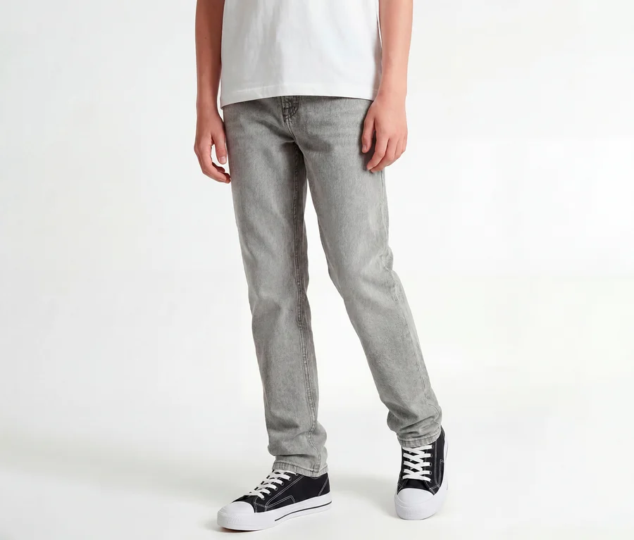 Stojící osoba v bílém tričku, šedých džínách Jack & Jones JJOriginal Chris a černých teniskách.