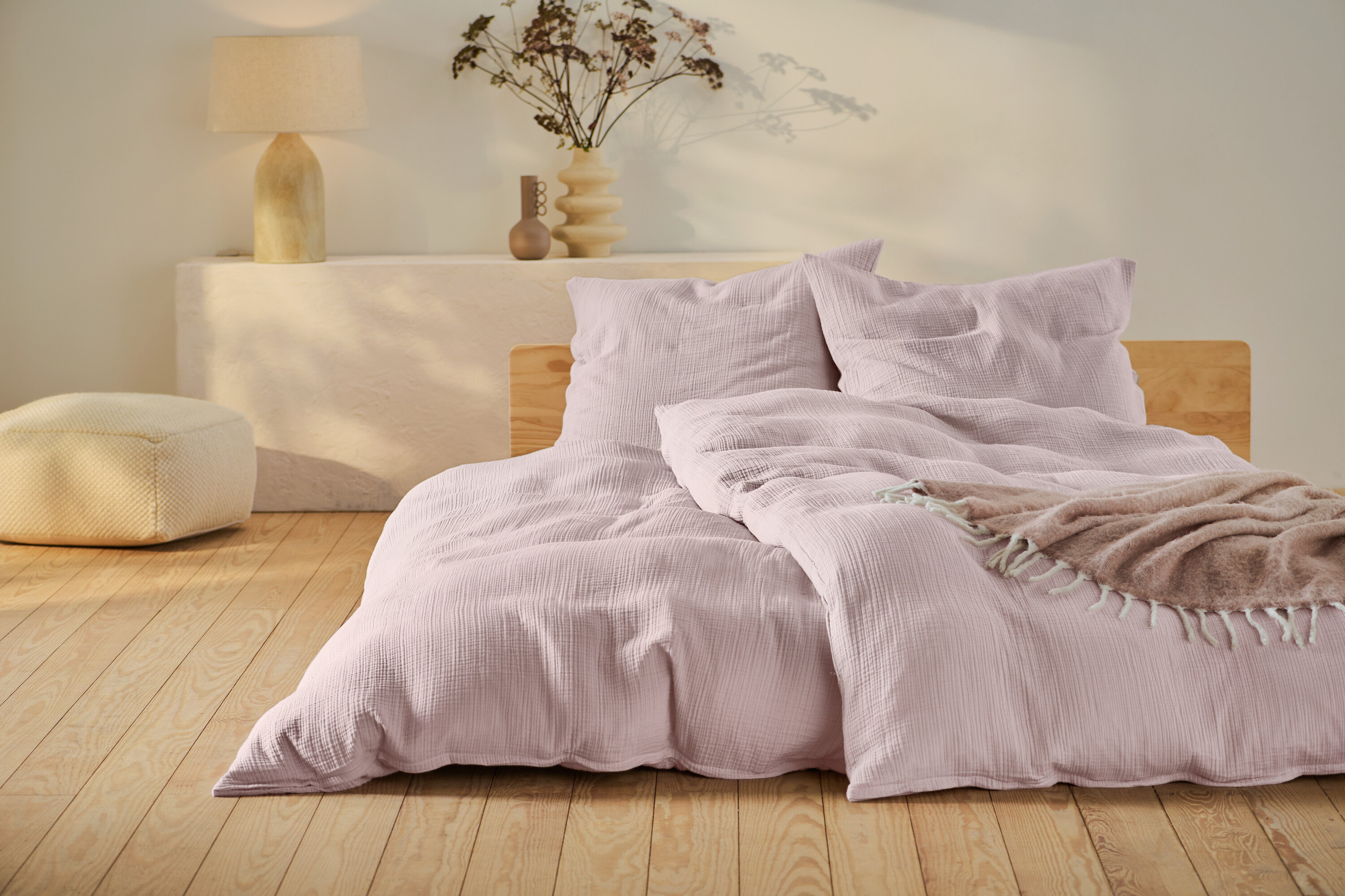 Růžové mušelínové povlečení standardní a nadměrné velikosti na posteli s dřevěným rámem.