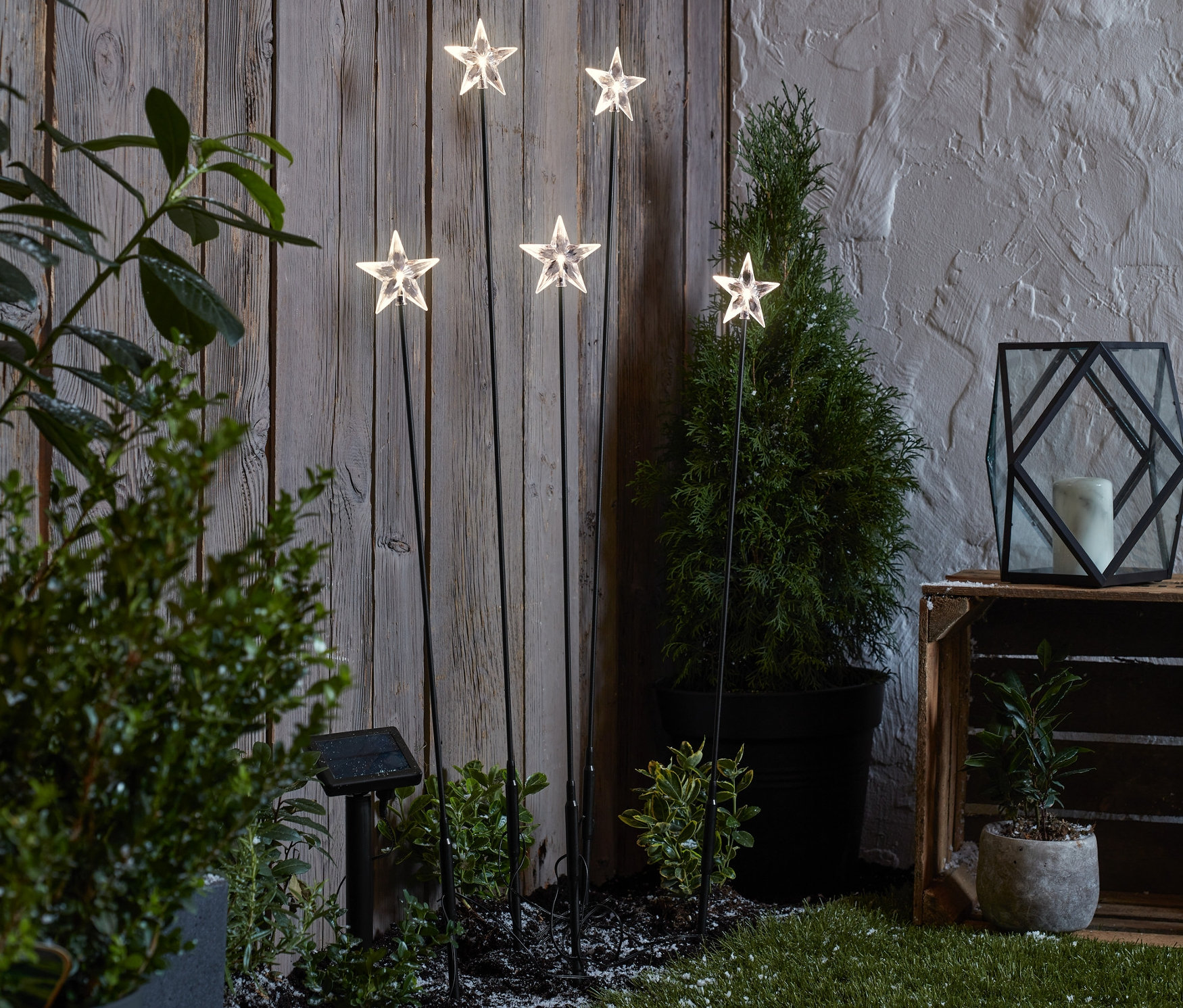 Pět solárních zápichů ve tvaru hvězdy stojí na trávníku před dřevěným plotem.