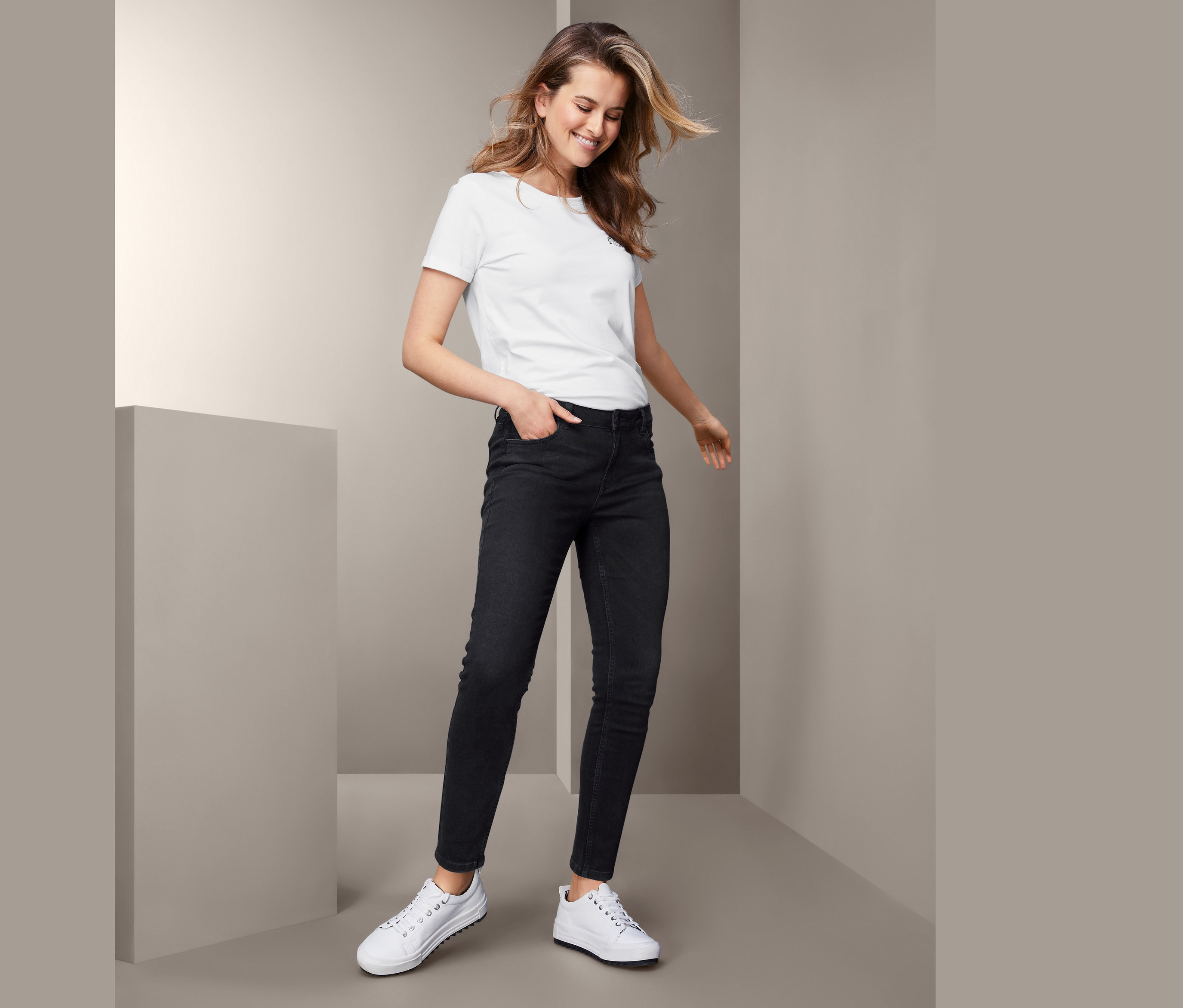 Žena pózuje v černých úzkých džínech a bílém tričku.