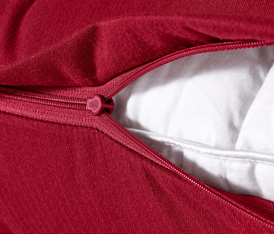 Detail červeného mikroflanelového povlaku na polštář s rozepnutým zipem, 80 x 40 cm, odhalující bílou výplň.