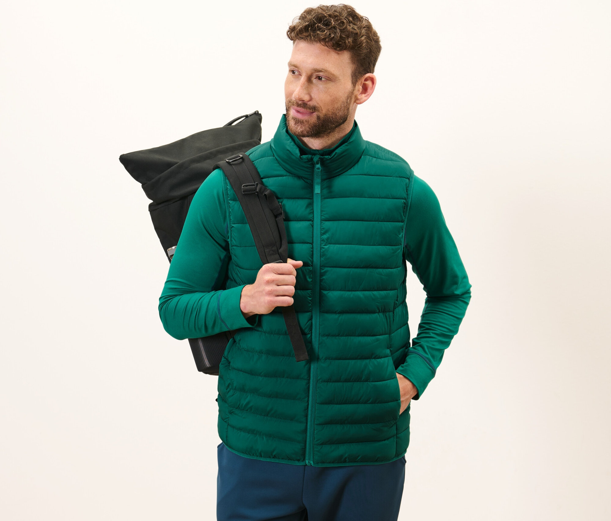Muž má na sobě zelenou prošívanou vestu Skladná prošívaná vesta a nese černý batoh.