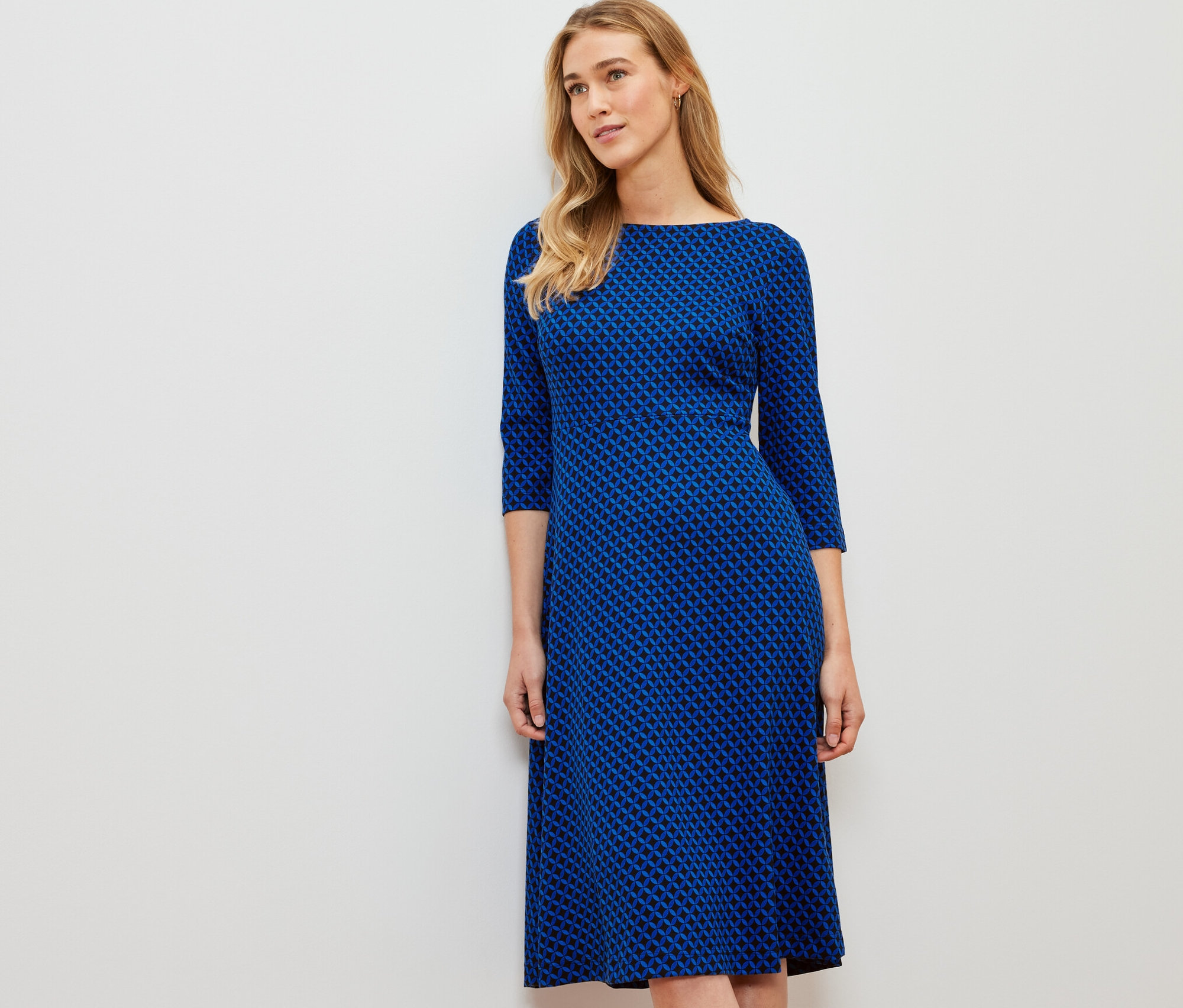 Žena stojí a má na sobě žerzejové šaty s potiskem.
