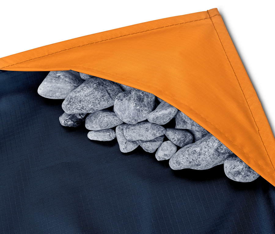 Detail mini deky na piknik s oranžovým lemem a hromadou kamenů.