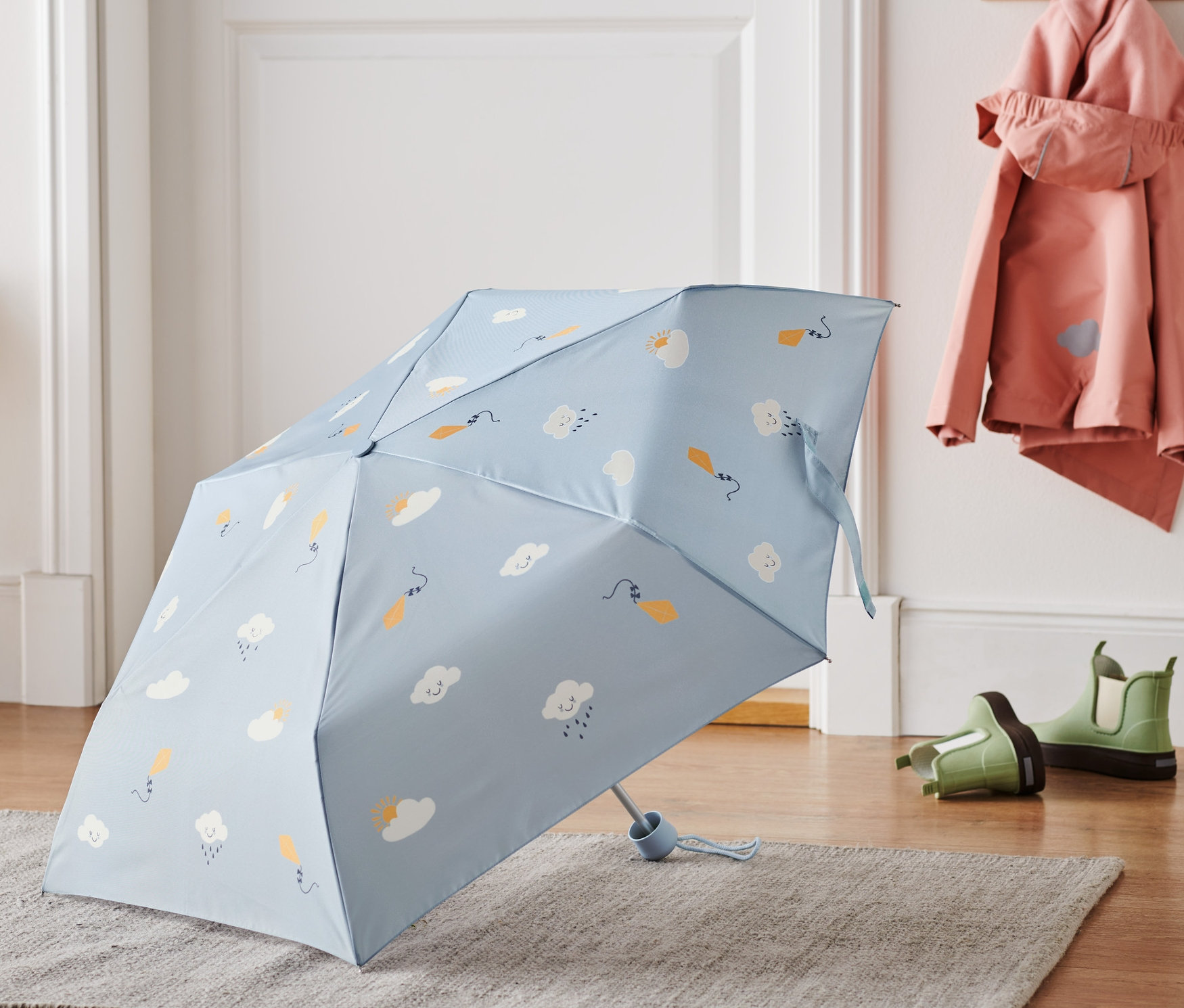 Modrý dětský deštník s motivem obláčků leží na šedém koberci.