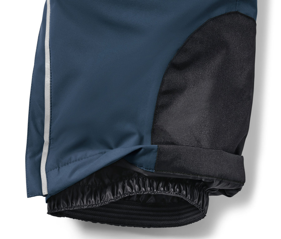 Detail dětských lyžařských kalhot námořnické modré barvy s černou látkou na kolenou a bílým pruhem na boku.