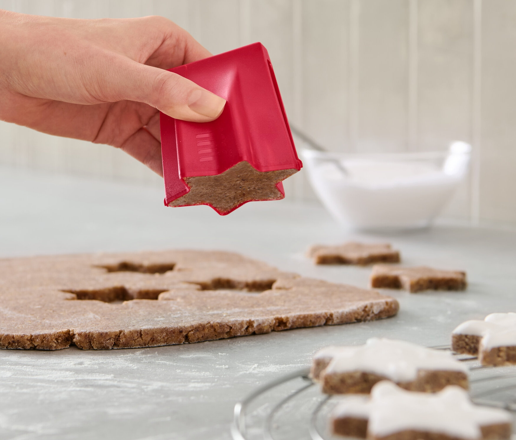 Ruka používá vykrajovátko na skořicové hvězdičky na těsto. Na lince jsou hvězdičky s polevou a mísa s polevou.