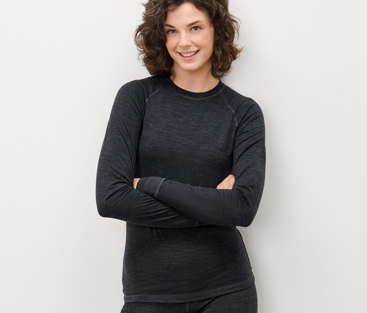 Žena se zkříženýma rukama pózuje v šedém funkčním triku s vlnou s certifikací RWS a kalhotách.