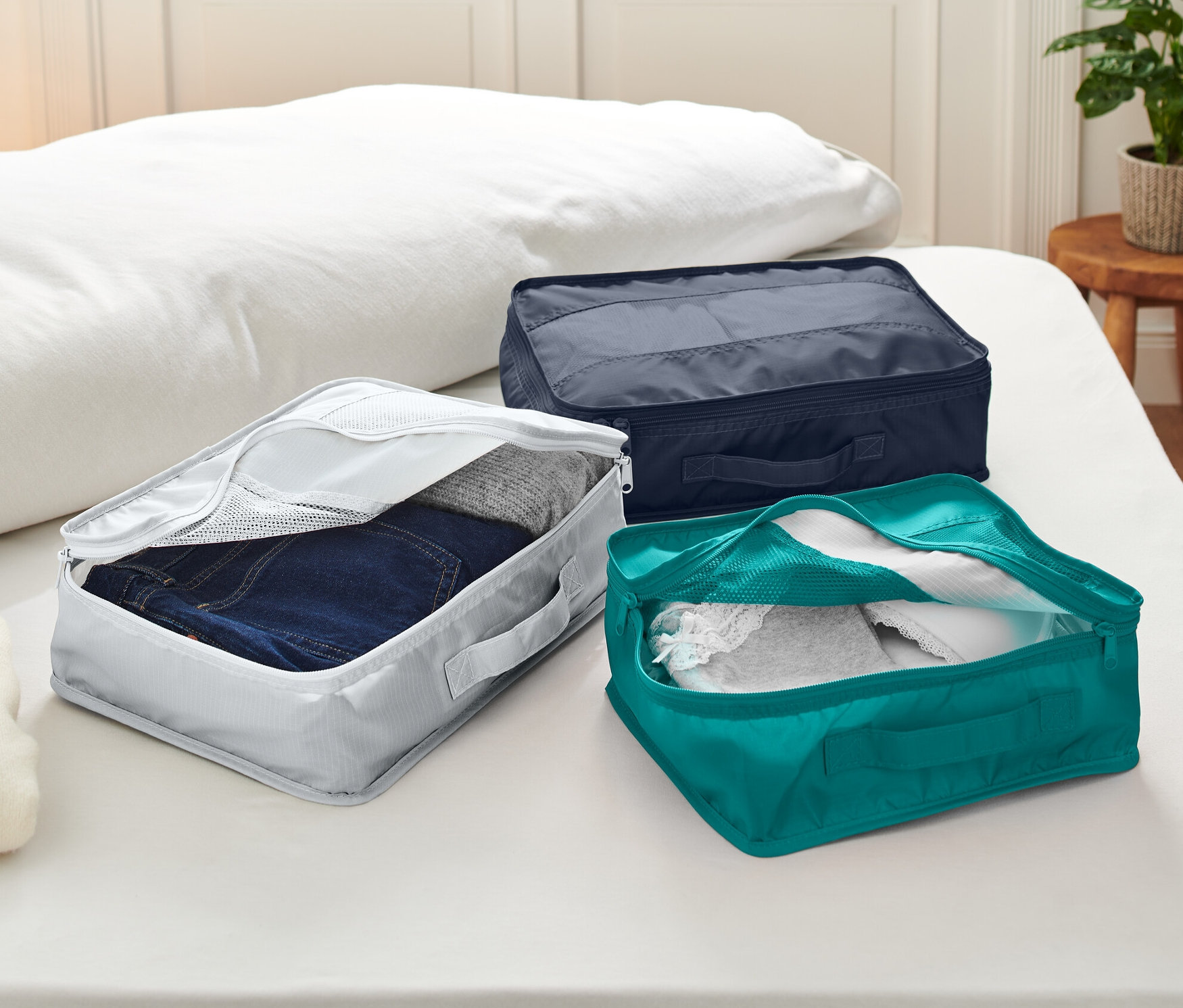 Tři cestovní úložné tašky leží na posteli.