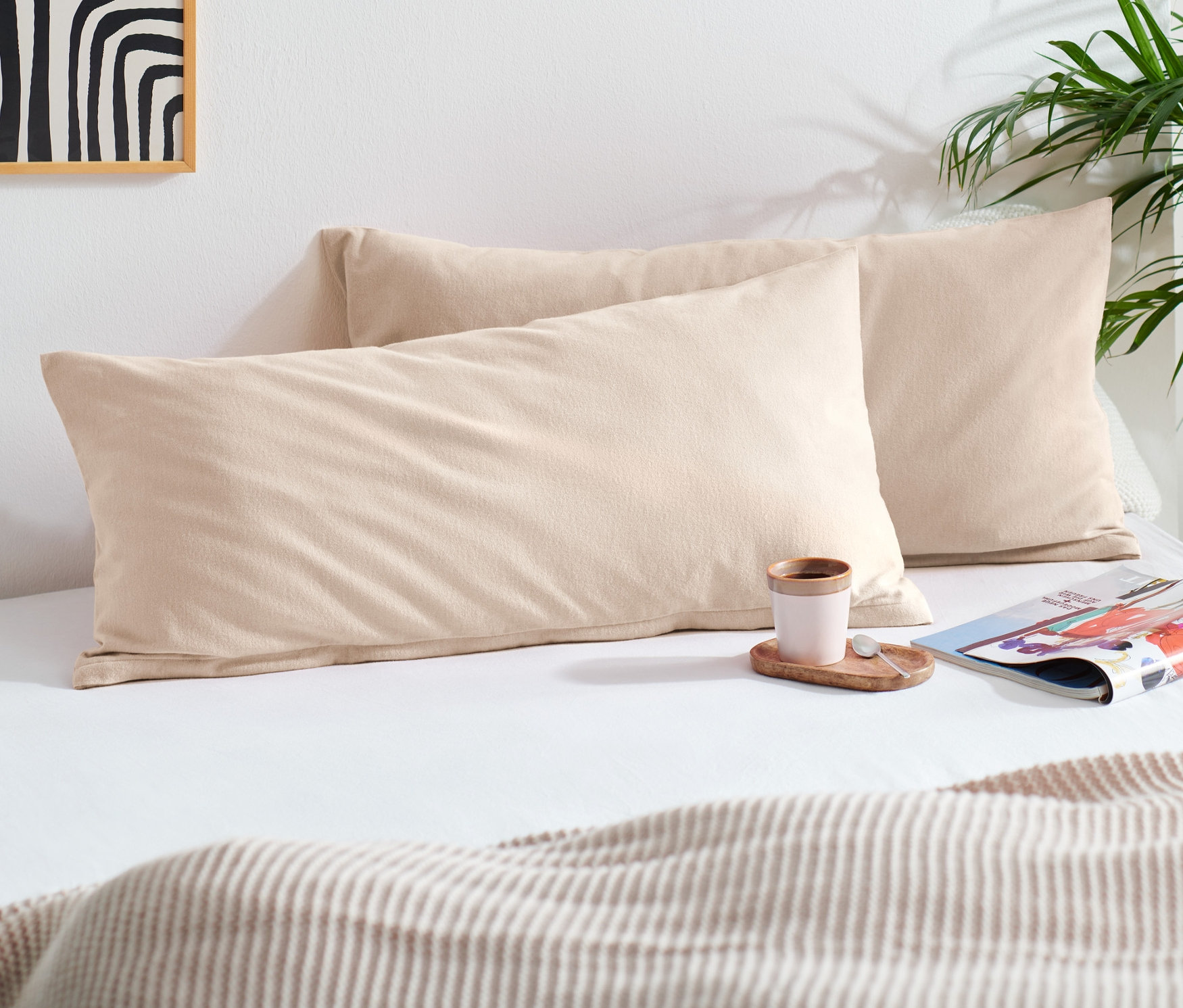 Dva béžové flanelové povlaky na polštáře leží na posteli vedle sebe.