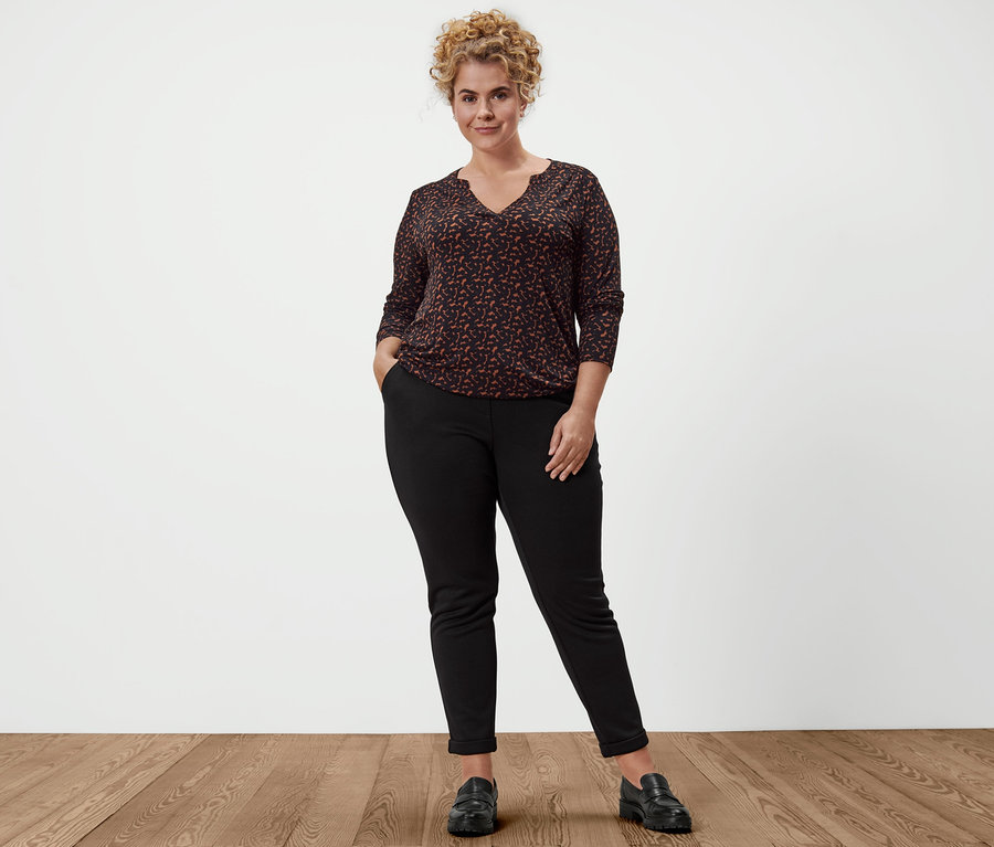 Žena pózuje v pohodlných kalhotách, kožených mokasínech a halenkovém triku s potiskem.