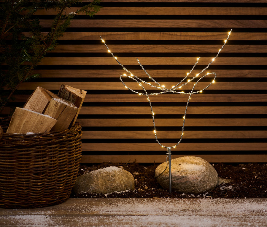 LED sobí hlava stojí venku mezi kameny a košem s dřevem.