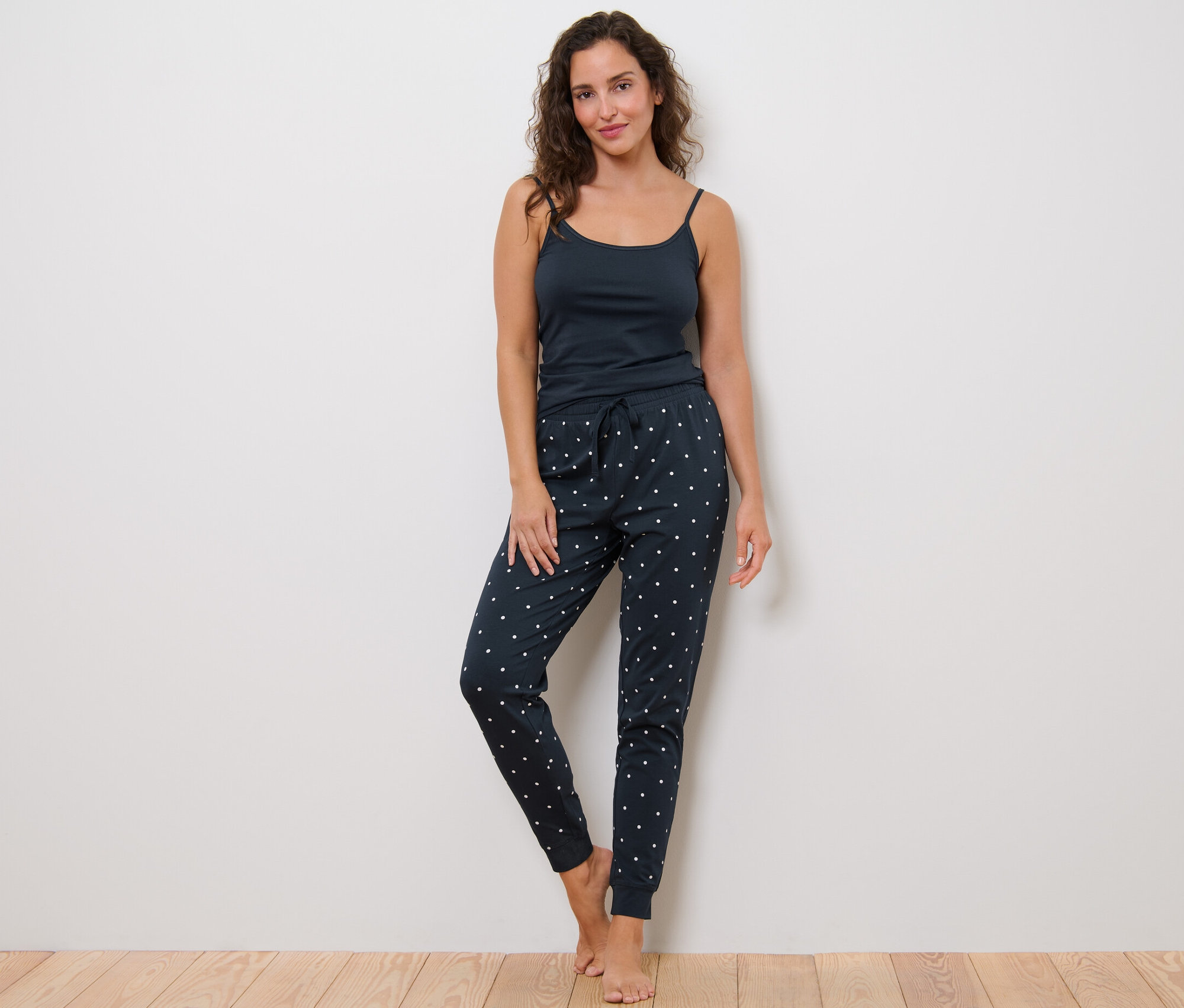 Žena stojí a má na sobě pyžamové kalhoty s puntíky a top.