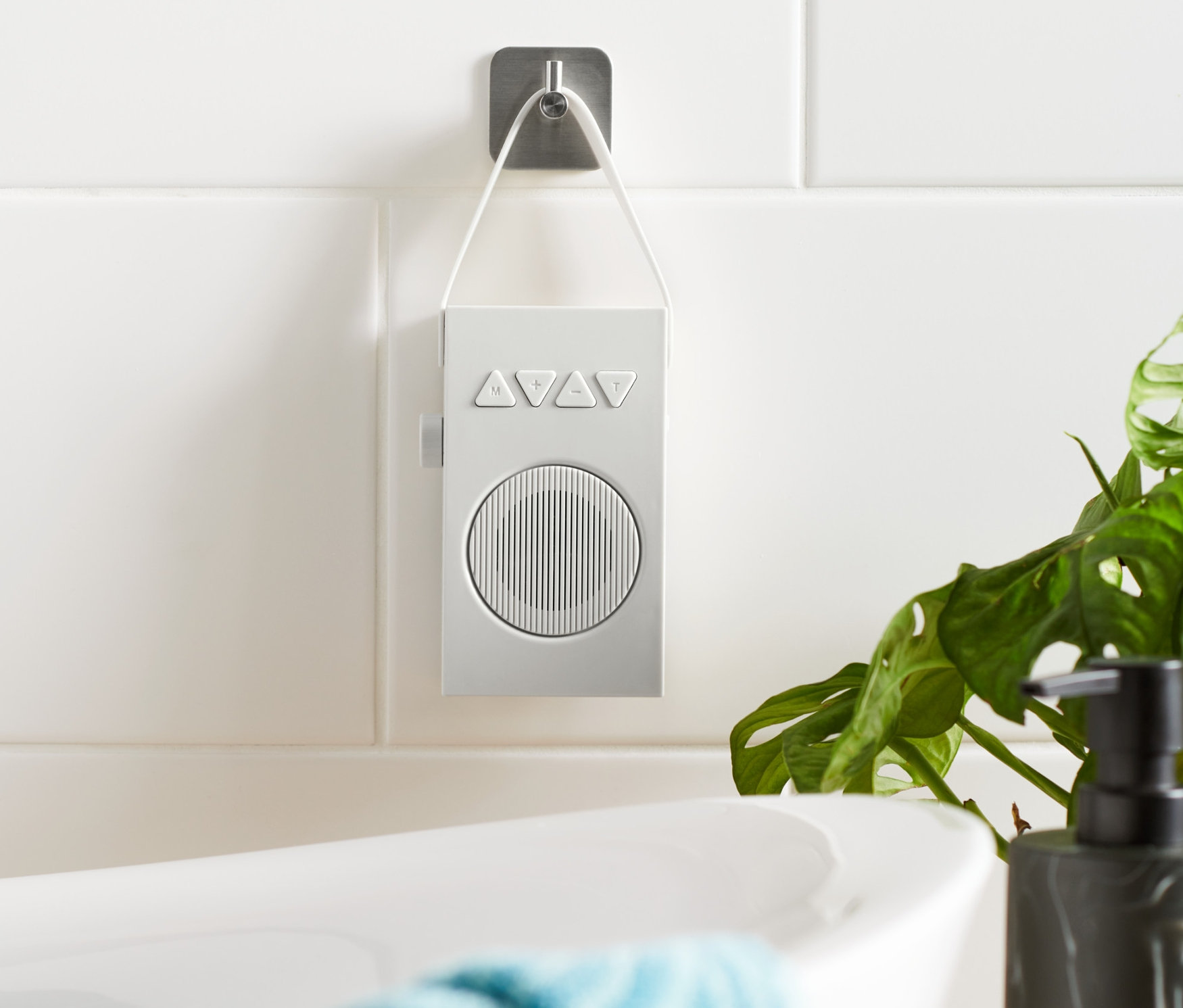 Bílé koupelnové rádio visí na dlaždicové zdi vedle vany.