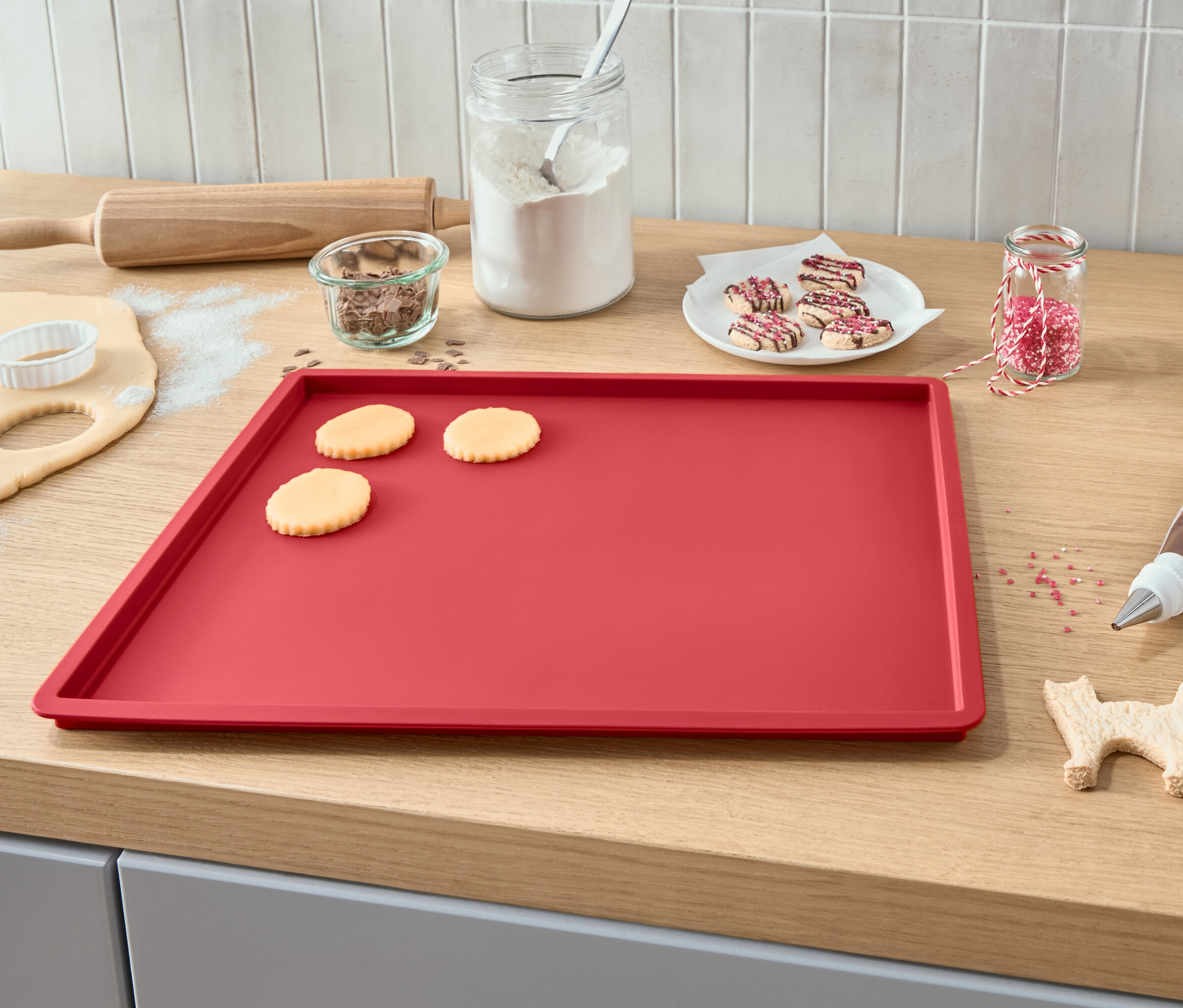 Plech na pečení s rozváleným těstem, vykrájenými sušenkami, polevou, posypem a válečkem.