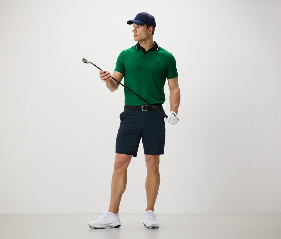 Muž drží golfovou hůl a má na sobě funkční šortky.