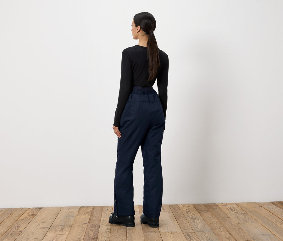 Žena stojí zády k fotoaparátu a má na sobě černé tričko s dlouhým rukávem a tmavě modré kalhoty.