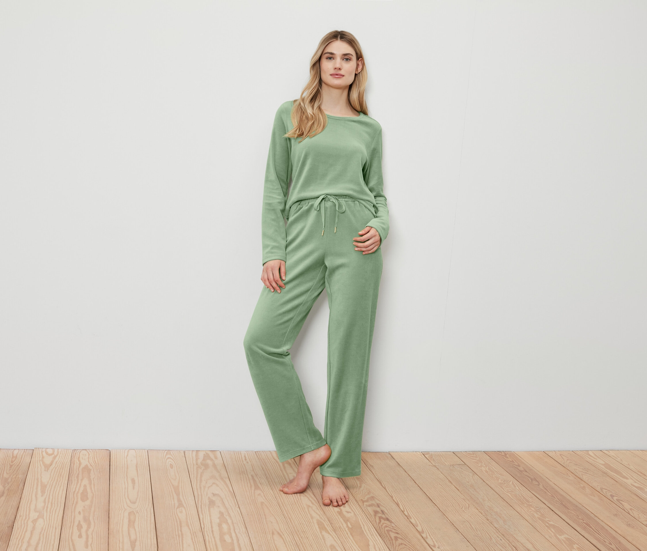 Žena pózuje v zeleném svetru a kalhotách.