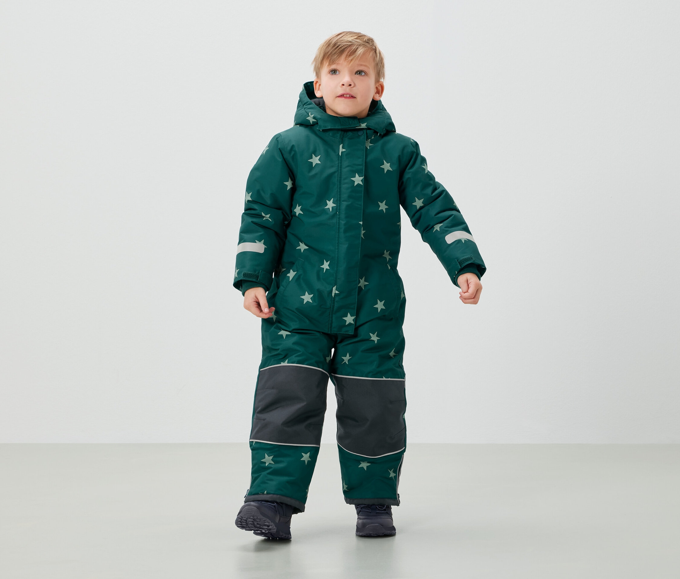 Chlapec v zelené kombinéze s hvězdami stojí.