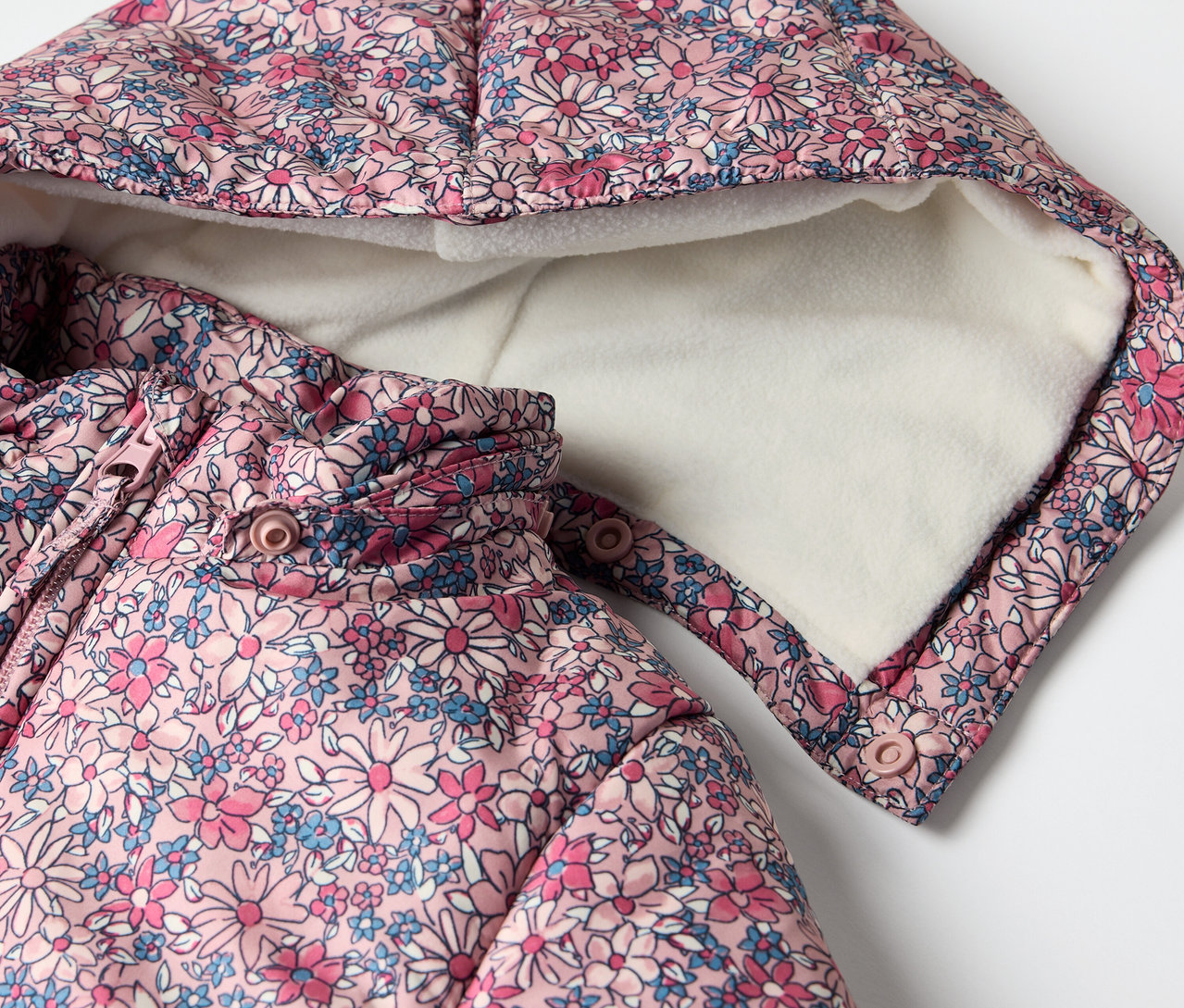 Detail zimního overalu pro miminka s květinovým vzorem a kapucí.