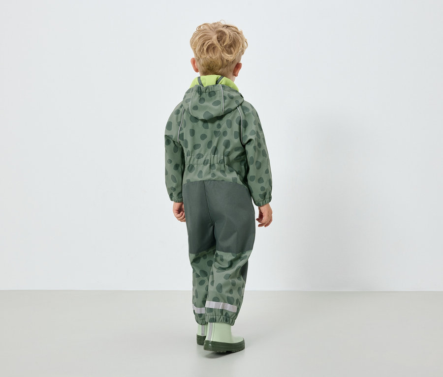 Chlapec v zelené kombinéze s kapucí, zády k fotoaparátu.