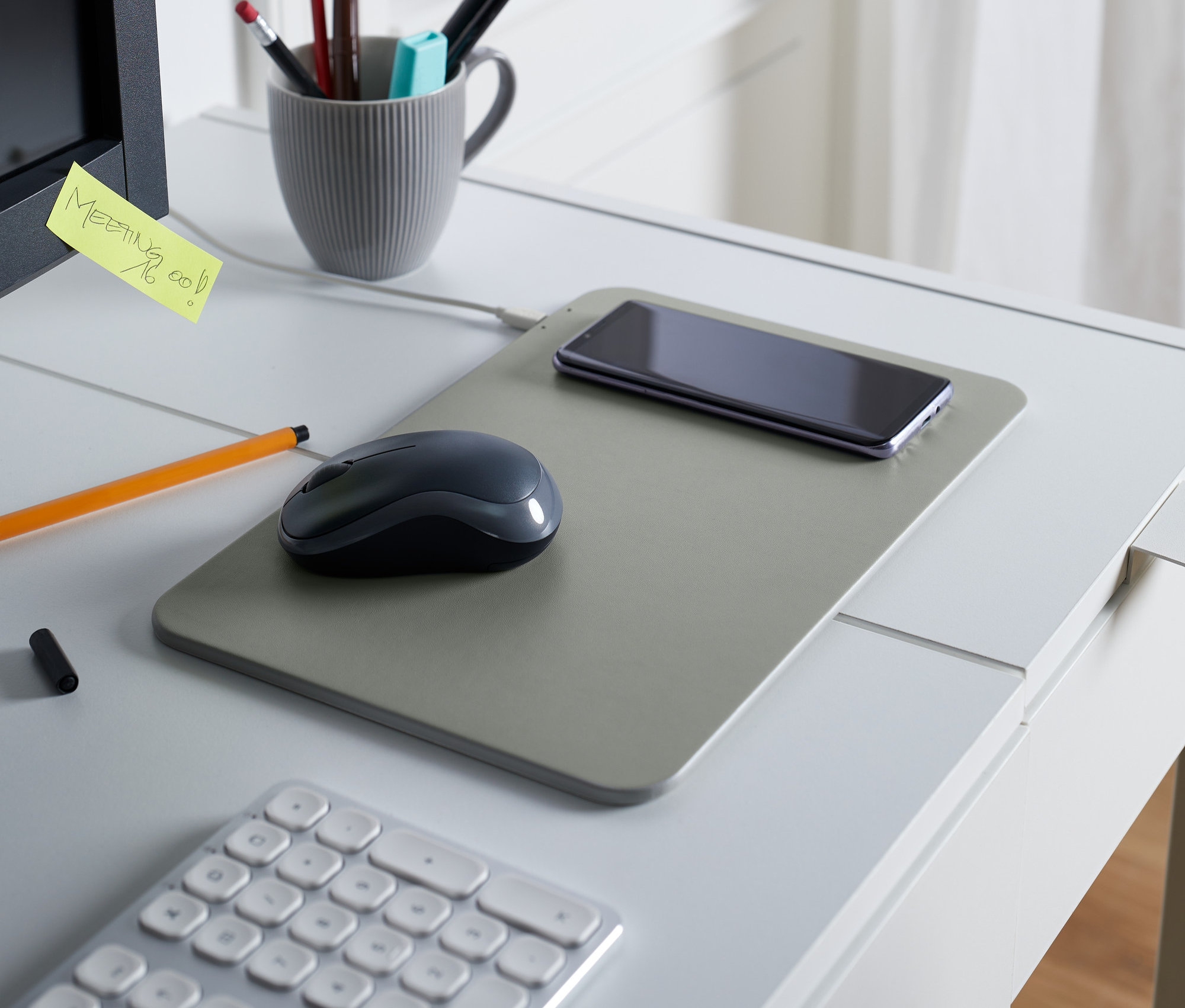 Na stole leží podložka pod myš s bezdrátovou nabíječkou, myš a telefon.