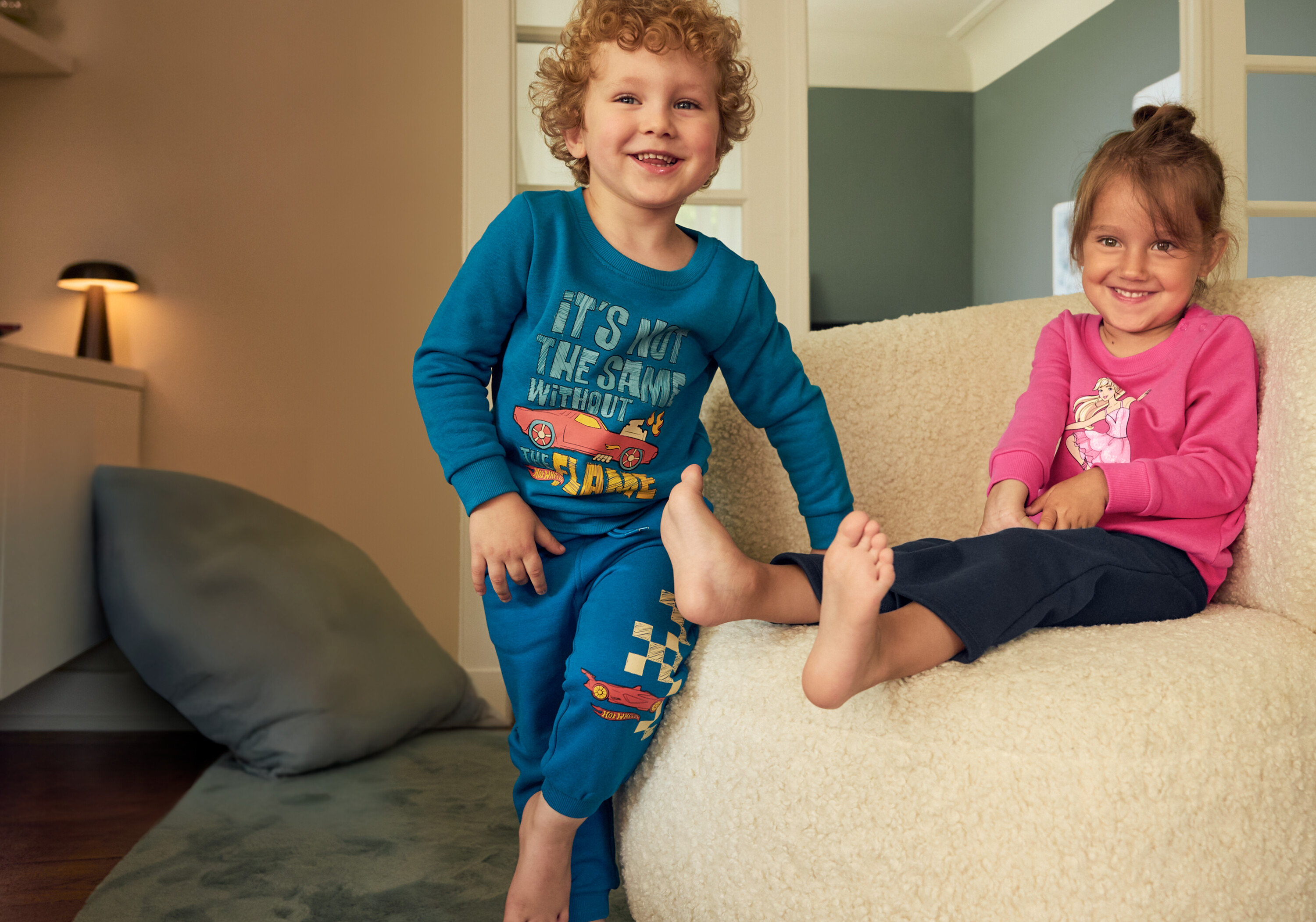 Chlapec v modrém kompletu a dívka v růžovém sedí na béžovém křesle. Chlapec má na sobě 2 ks dětských termo legín s vnitřní stranou.